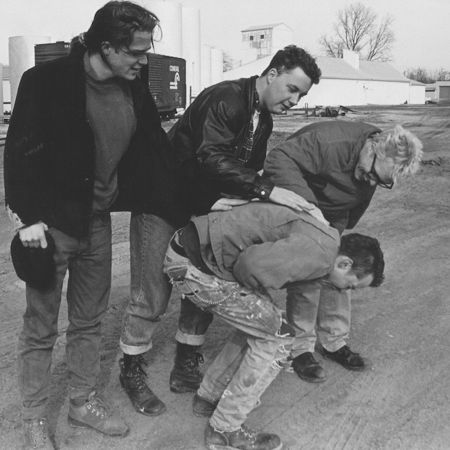 The members of Ugly Stick stand against a weathered Ohio backdrop, guitars in hand, exuding the defiant cow-punk energy that defined their 1993 cult classic Absinthe, now reborn on vinyl.