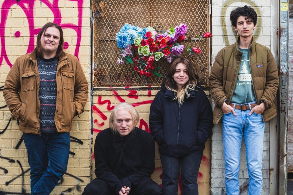 Band photo of NYC’s Star Card by Katixa Espinoza, featuring Calley front and center with guitar in hand, framed in dim natural light that mirrors the vulnerable and gritty mood of their new single “Flowers.”