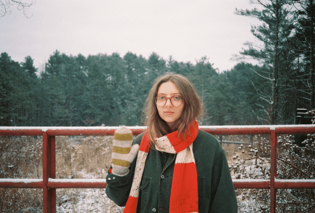 runo plum stands in soft light near a still pond, her reflection merging with the water as dusk falls — a visual echo of the quiet introspection that defines her new single “Pond.”