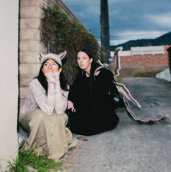 Disiniblud’s Rachika Nayar and Nina Keith stand against a surreal, glowing backdrop while Kelly Moran performs on piano — a visual echo of their hauntingly beautiful remix EP, where ambience meets chaos in “Blue Rags, Raging Wind.”